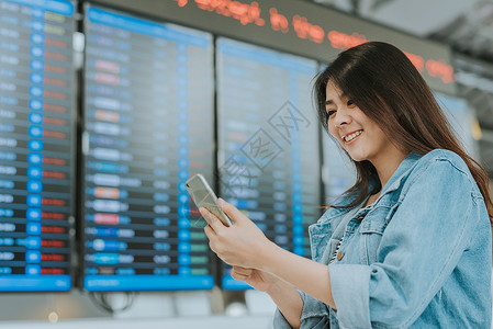快乐的亚洲女在机场使用智能手机背景图片