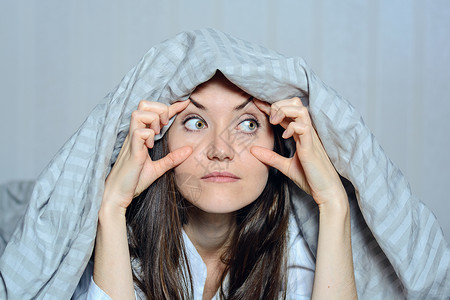 一名患有失眠症的妇女用手捂住眼睛的特写正面肖像图片
