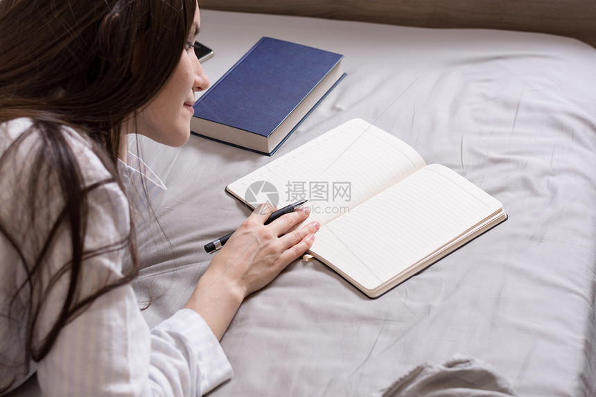 一个黑发女人背着一本书和一本日记躺在床上的肖像图片