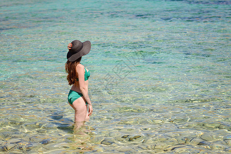 身戴黑帽子绿色泳衣站在绿宝石海水里复制空间和侧视的褐图片