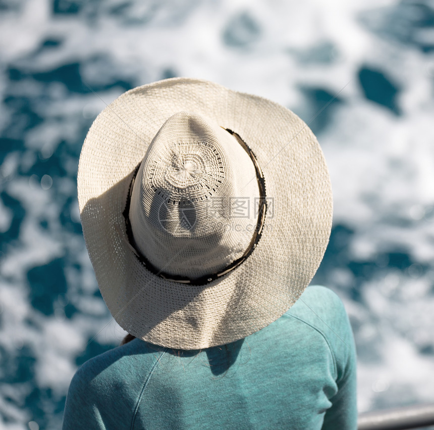 戴着帽子的陌生女人看着海洋就像度假概图片