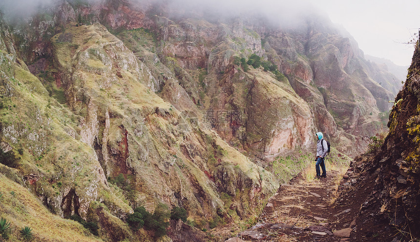男徒步旅行者在通往著名保罗谷的陡峭岩石小路上欣赏令人印象深刻的山面SantoAntao佛图片