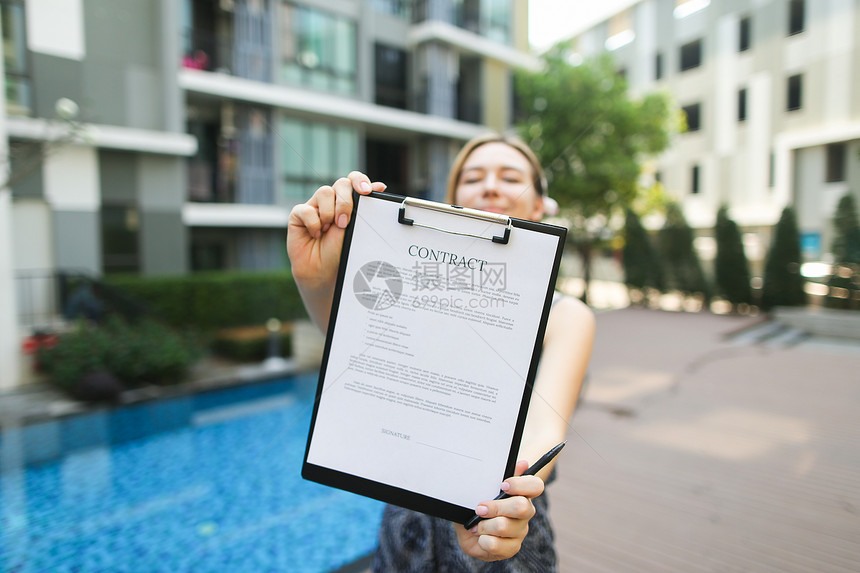 女手拿出钢笔和合同签字建筑背景上的阳光肖像与新公寓游泳池和阳光正面与开放字体许图片
