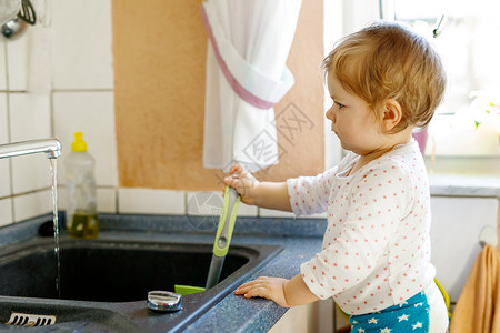 可爱的金发小女婴在家用厨房洗盘子图片