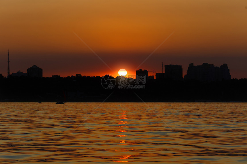 美丽的海景靠近海岸线的海中明亮温暖的日落与城市的轮廓太阳躲在房子后面天空的颜图片