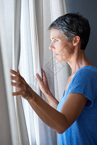 老妇人拉开窗帘望向窗外的肖像图片