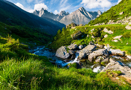 岩石间的狂野溪流美丽的复合景观与草山在夏天远处有岩石山峰的山脊图片