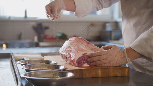 屠夫把香料添加到大块新鲜生肉中躺在一家餐饮烹饪和上菜商业厨图片