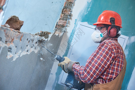 在建筑行业打破内部砖墙施工服务的带有个人防护设备和拆除锤的工人图片