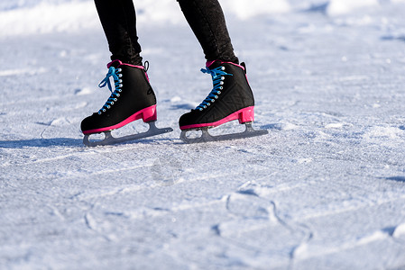 穿着黑大衣在冰冻湖上溜冰的年轻女孩用现代滑雪鞋在雪图片