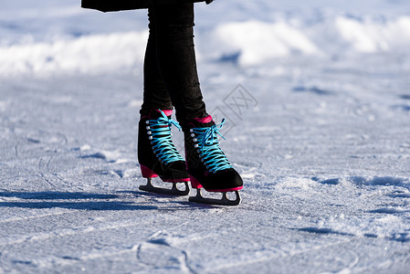 穿着黑大衣在冰冻湖上溜冰的年轻女孩用现代滑雪鞋在雪图片