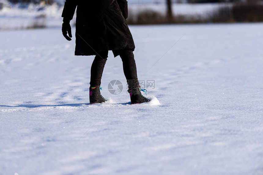 穿着黑大衣在冰冻的湖边滑雪的年轻女孩与现代溜冰鞋一起下雪图片