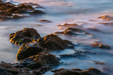 日落时海和岩石的长时间曝光图片