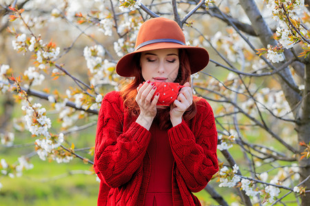 红衣帽的红发女孩拿着咖啡杯在花图片