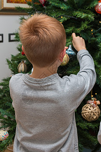 八岁男孩在圣诞树上挂球和装饰品图片