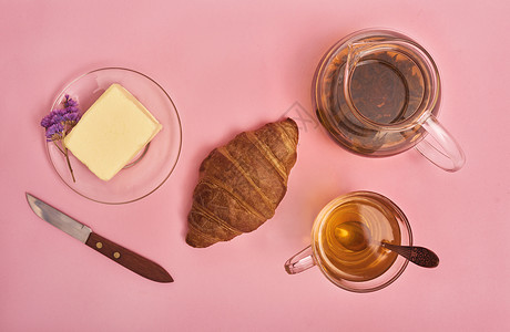 新鲜烘烤的美味羊角面包茶杯奶油刀子粉红背景的鲜图片