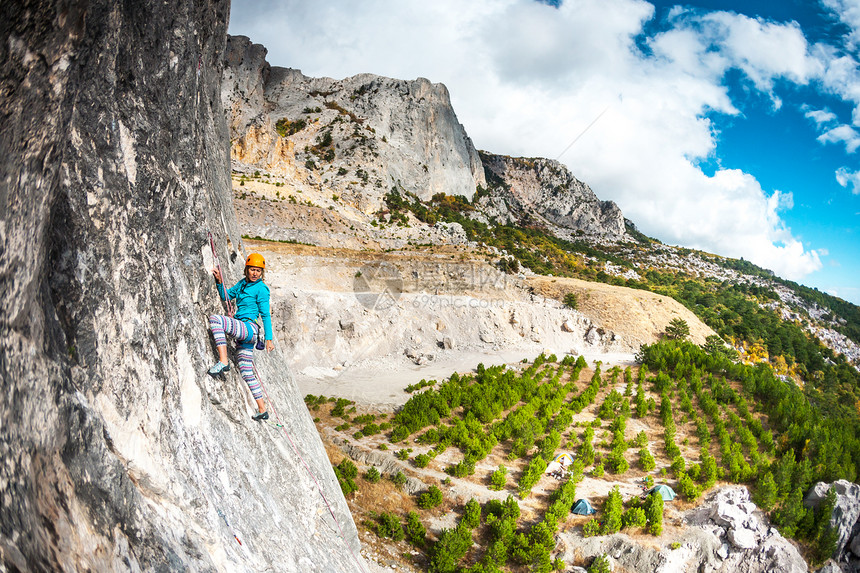岩石上的攀岩者戴头盔的女孩在美丽的山景和乌云密布的天空的背景下爬上岩石自然运动克服困图片