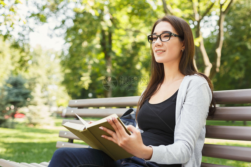 戴眼镜的年轻微笑女人在公园看书图片
