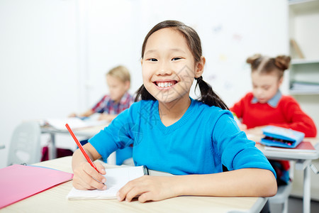 带着牙齿笑的漂亮女学生在上课时坐在个别座位上看着图片