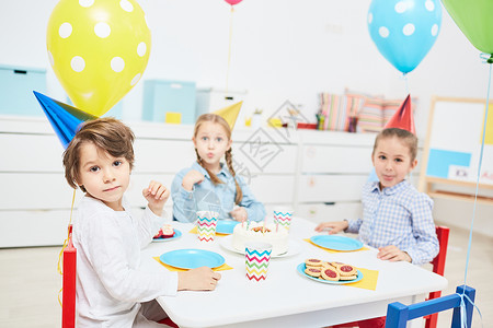 一群穿着生日帽子的可爱孩子坐在节日桌边图片