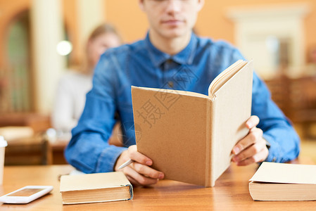无法辨认的图书馆访客坐在木制桌子和阅读书旁图片