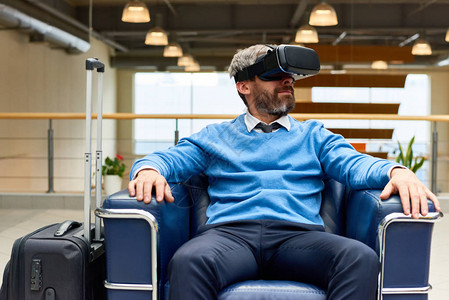 戴着VR耳机的成熟胡须男子坐在扶手椅上沉浸在游戏中环图片
