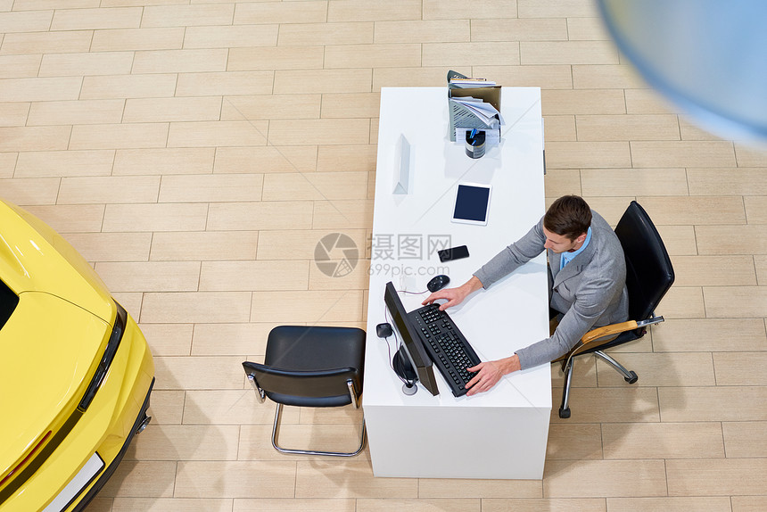 上面是英俊的售货员坐在桌子上用电脑在空展厅用电图片