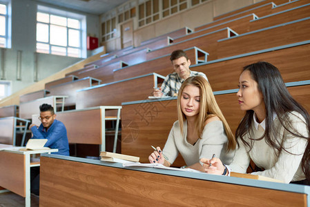 国际人群坐在现代大学报告厅的不同桌子上图片