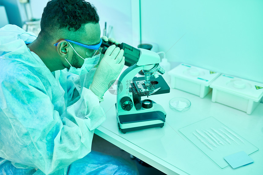年轻中东科学家在实验室进行医学研究时使用显微镜的侧面画像照片用图片
