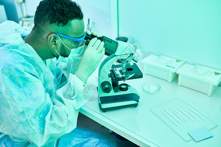 年轻中东科学家在实验室进行医学研究时使用显微镜的侧面画像照片用图片