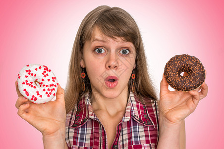 迷人的女人在两个甜圈之间做出抉择与粉背景图片