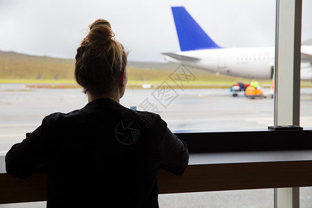 中成年妇女透过机场窗户看飞机的近视图片