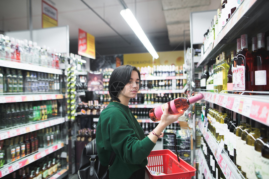 一个漂亮的女孩在超市购物时仔细地看着酒瓶这个女孩读了一个酒标图片