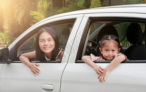 快乐的年轻女人和她的小女儿坐在后座上家庭旅行的概念图片