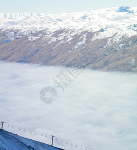 缆车从雾谷中升起缆车是空的背景是被雪覆盖的山脉天空是蓝色图片