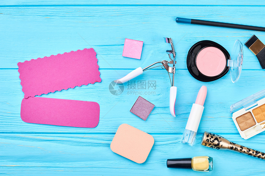 在蓝色背景上设置的五颜六色的化妆品装饰化妆品必需品和化妆工具文本的粉红色纸卡美图片