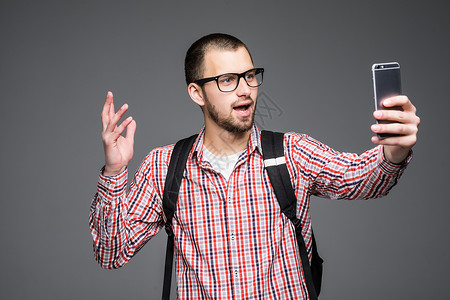 快乐的年轻人在灰色背景上通过智能手机拍摄自我肖像摄影图片