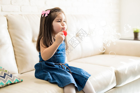 小女孩坐在沙发上在客厅吹肥皂泡图片