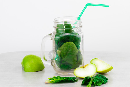 玻璃罐中的绿色冰沙与灰色背景的新鲜有机绿色蔬菜和水果图片