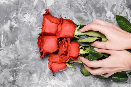五朵红玫瑰在女手中在灰色混凝图片