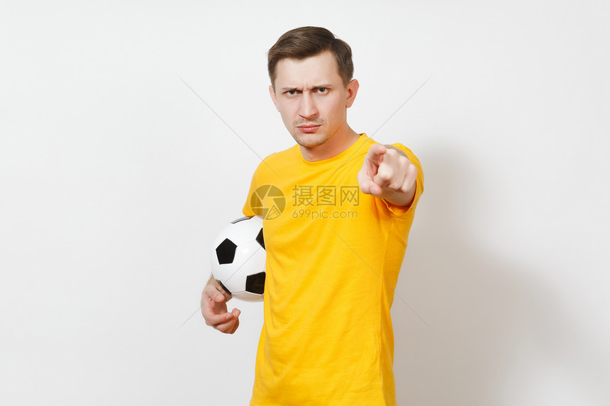 年轻的愤怒的欧洲男子球迷或身穿黄色制服的球员拿着足球点食指相机欢呼最喜欢的足球队图片
