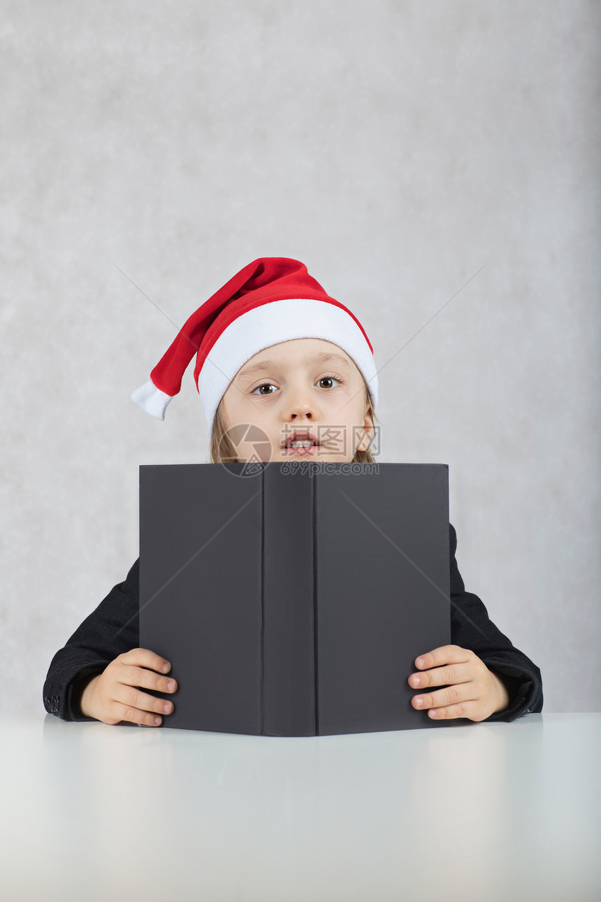 圣诞老人的帽子和黑色古典夹克的四年男孩在圣诞老人的帽子和黑书的四年的特写镜头男孩坐图片