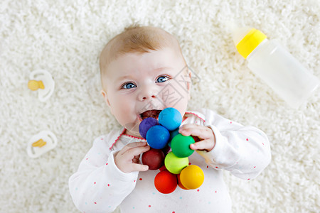可爱的新生婴儿在玩五颜六色的木制拨浪鼓玩具哺乳奶瓶和假人背景图片