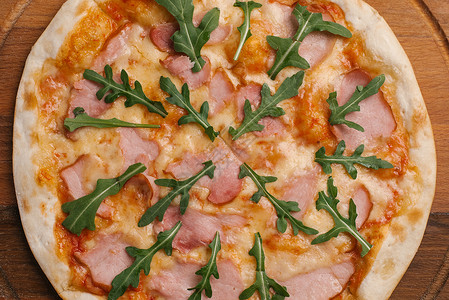 用番茄酱奶酪火腿和芝麻菜在木制比萨盘上供应比萨的近景图片