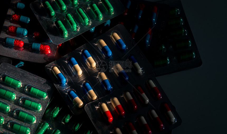 一堆五颜六色的胶囊丸在深色背景的吸塑包装中药物政策和预算合理使用抗生素药物抗生素耐药概念图片