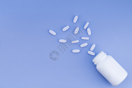 从瓶子上撒出的药片放在蓝色面糊的蓝背景上文字的位图片
