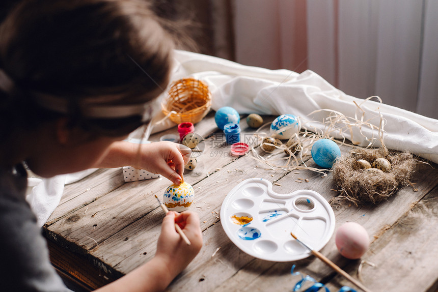 用刷子蓝色和黄色的圆点在木桌上用艺术工具将儿童手握着和彩蛋并涂图片