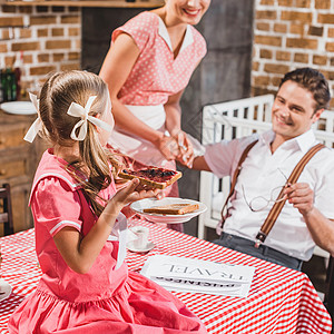 笑着看可爱的女儿在1950年代式家庭早餐时用果酱吃烤图片