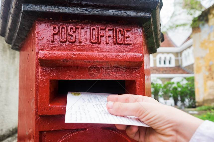在将一封信放入红色信箱的男手上的特写老式通信类型的概念从假期或旅行图片
