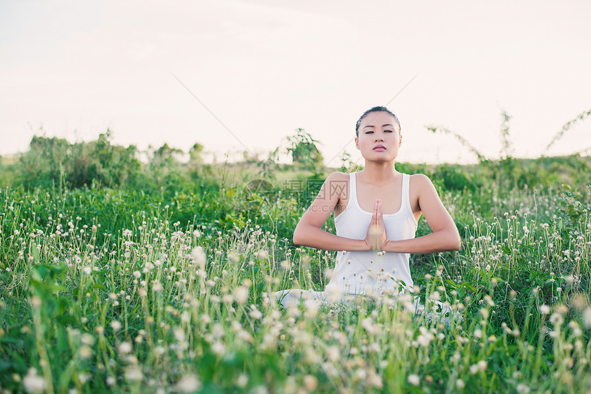 美丽的年轻瑜伽女子坐在草原上手图片